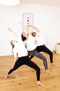 3 Personen in einer Reihe stehend in der Position des Umgekehrten Kriegers, im Raum der Yogaria, eine dynamische Yogapose