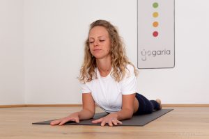 Magdalena auf ihrer schwarzen Yogamatte in der Position Sphinx vor dem Yogaria Logo