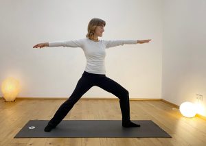 Bella in der Pose des Kriegers auf der schwarzen Matte in der Yogaria