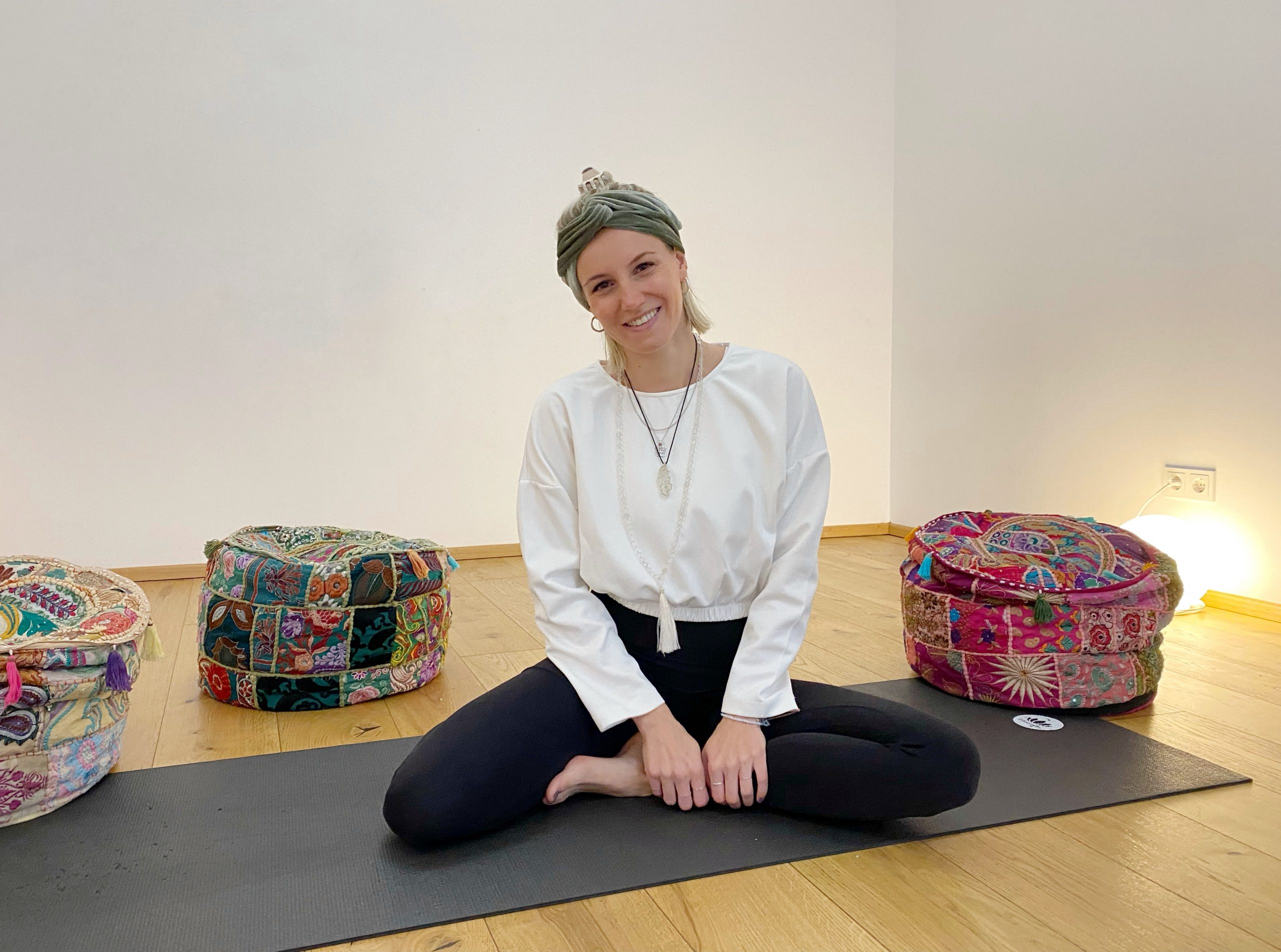 Kathi Wabnigg, sitzend und lächelnd auf einer schwarzen Yogamatte in der Yogaria