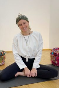 Kathi Wabnigg, sitzend und lächelnd auf einer schwarzen Yogamatte in der Yogaria