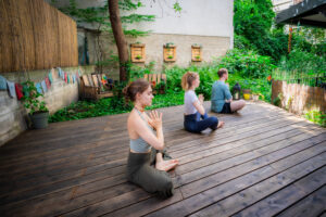 3 Yogis im Lotussitz mit gefalteten Händen vor der Brust, von der Seite fotografiert, im Garten der Yogaria
