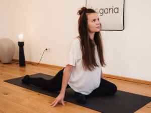 Barbara in der Pose der Taube oder Schwan. auf der schwarzen Yogamatte in der Yogaria