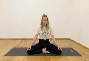 Marie meditativ sitzend auf dem grauen Block und der schwarzen Matte, ihre Augen sind geschlossen