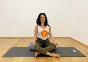 Anja meditativ sitzend auf dem grauen Yoga Bolster und der schwarzen Matte, Ihre Augen sind geschlossen