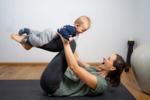 Mama und Baby sitzen auf der Yogamatte und machen Yoga