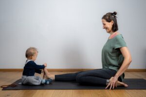 Mama und Baby sitzen auf der Yogamatte und machen Yoga
