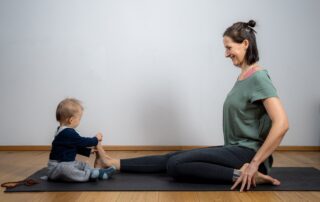 Mama und Baby sitzen auf der Yogamatte und machen Yoga