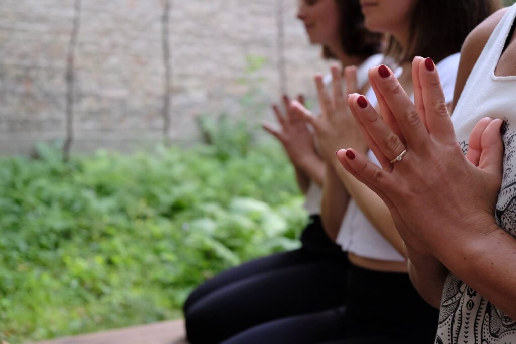 im Fokus des Fotos sind 3 paar Hände, gefaltet in Angeli Mudra oder auch Namaskar genannt, die Gebetshaltung im Yoga