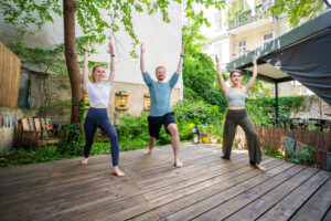 3 Yogis in der Position Krieger 1 mit erhobenen Händen im Garten der Yogaria