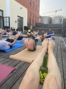 Man sieht die Beine von Gesichtspunkt der Bier Yogini, ein kleines Bier muss zwischen den Beinen festgehalten werden