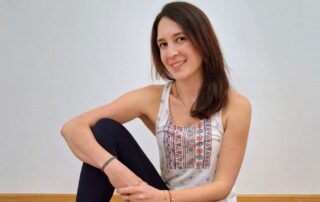 Denise sitzt auf einer Yogamatte und lächelt in die Kamera