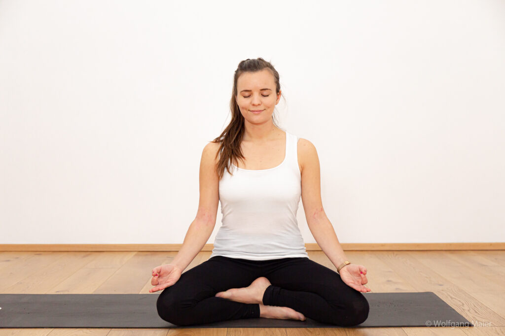 Barbara Gföllner sitzt im Lotussitz mit geschlossen Augen auf ihrer Yogamatte und meditiert