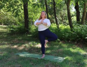 Asana ABC Nicole_Eversports Nicole in Tree Pose auf ihrer Matte im Grünen, dahinter ein wunderschöner Baum