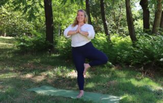Nicole in Tree Pose auf ihrer Matte im Grünen, dahinter ein wunderschöner Baum